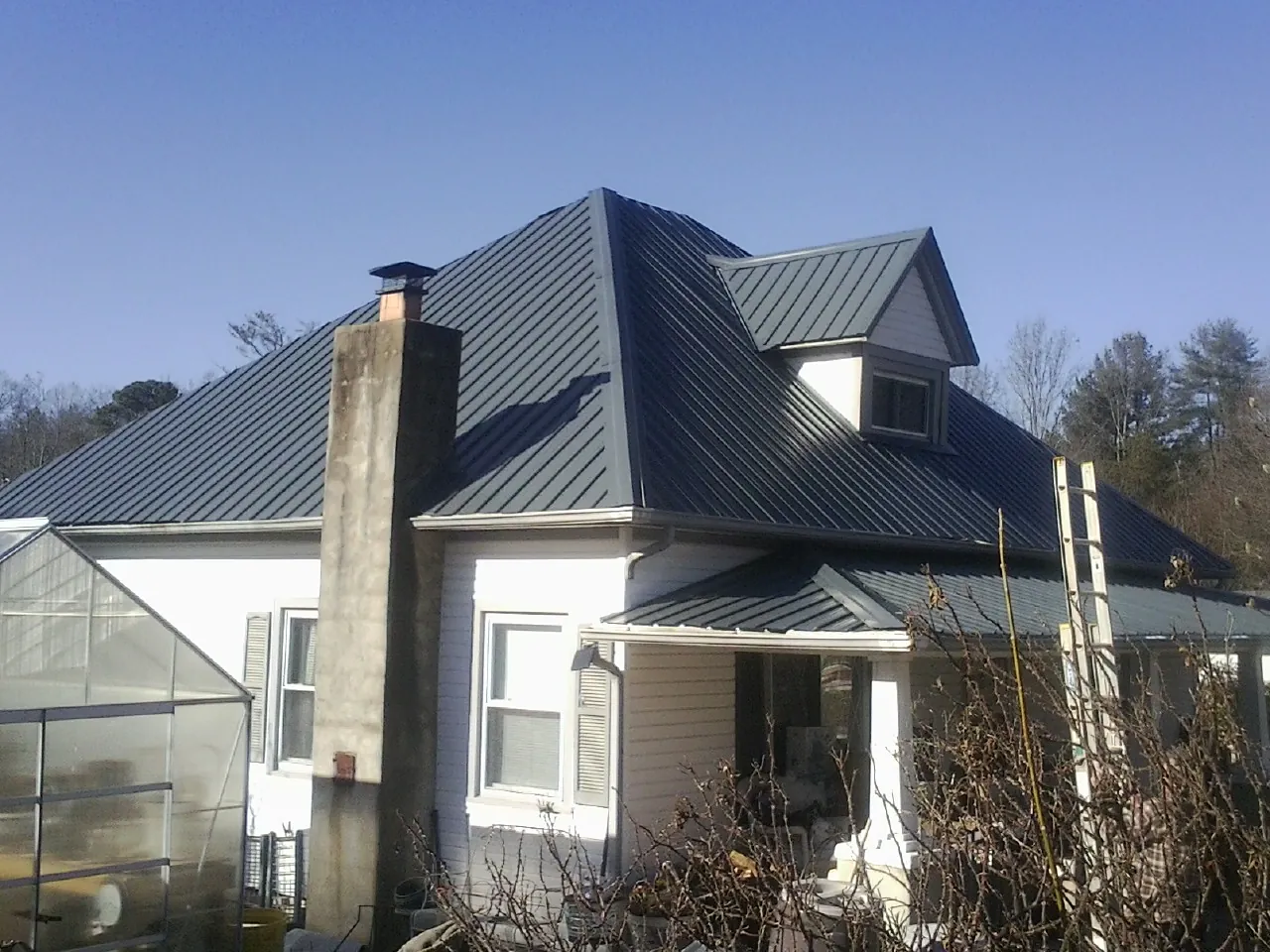 Dark blue standing seam metal roof on a white farmhouse with dormer — Slate & Tile Roof Repair by Roofing Brothers in Anniston