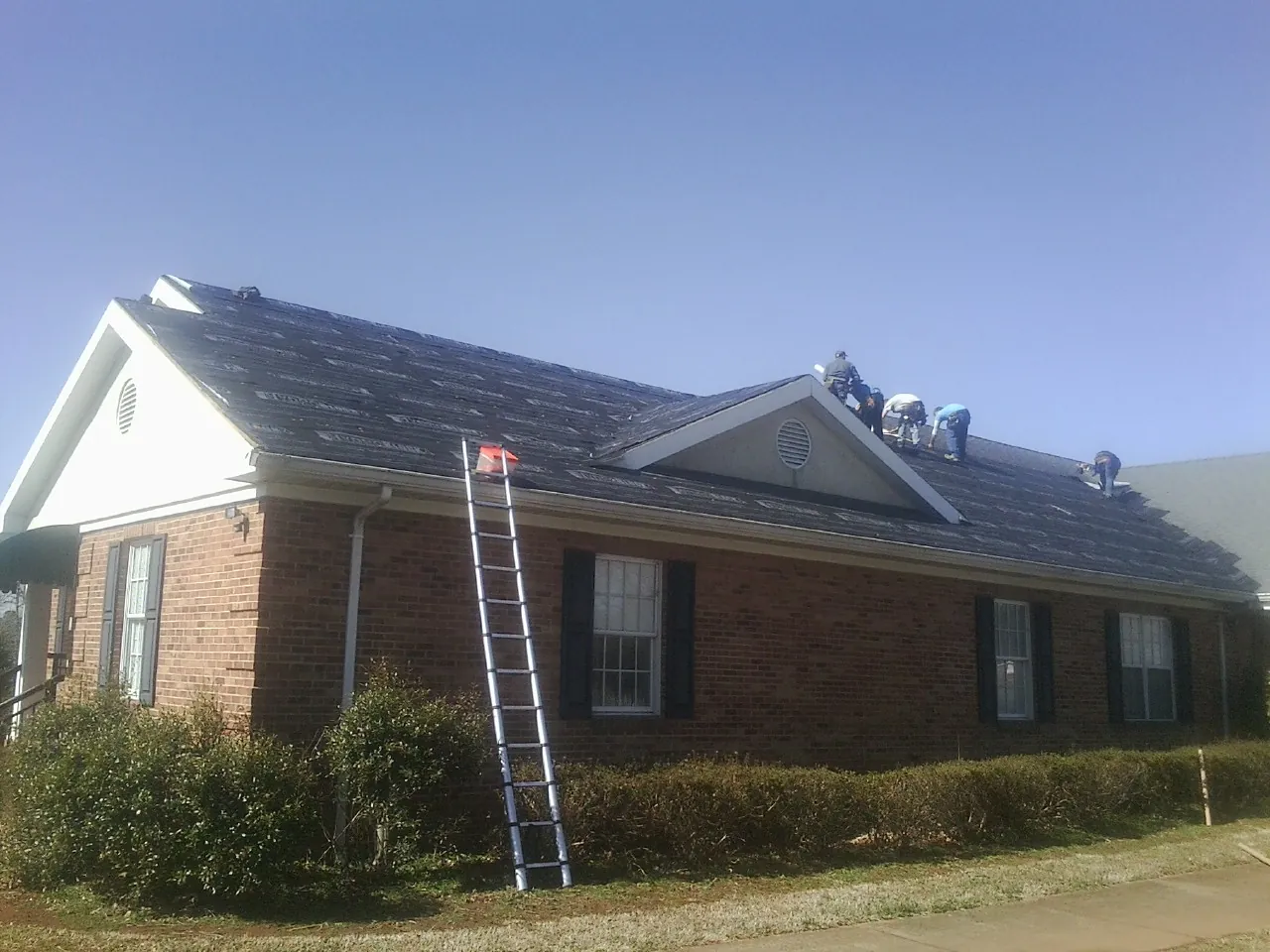 Crew tearing shingles off a brick ranch roof with a ladder set — Emergency Roof Repair work by our crew in Anniston