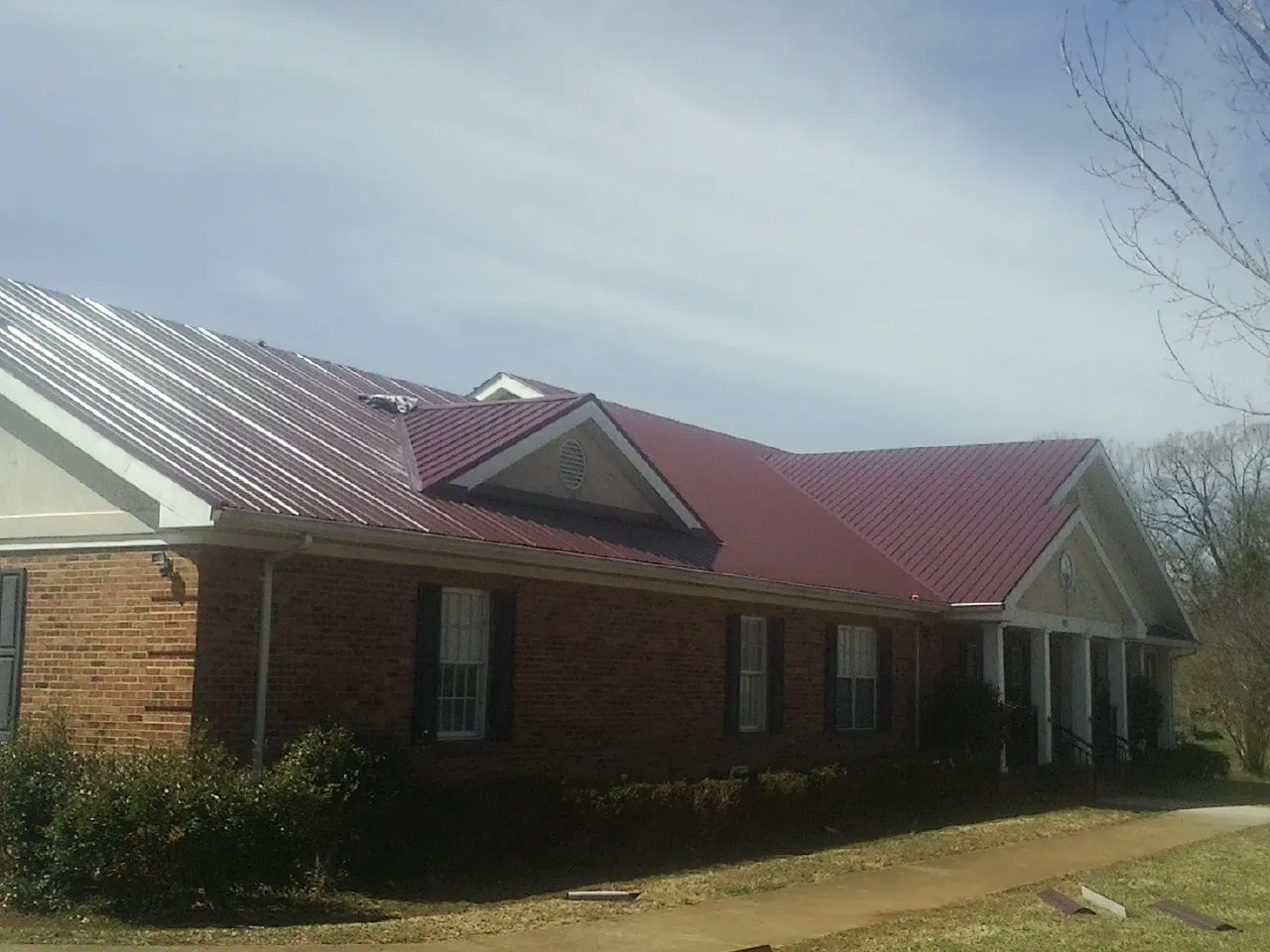 Red metal roof with gabled entries on a long brick building, from a Hail Damage Roof Repair job in Anniston