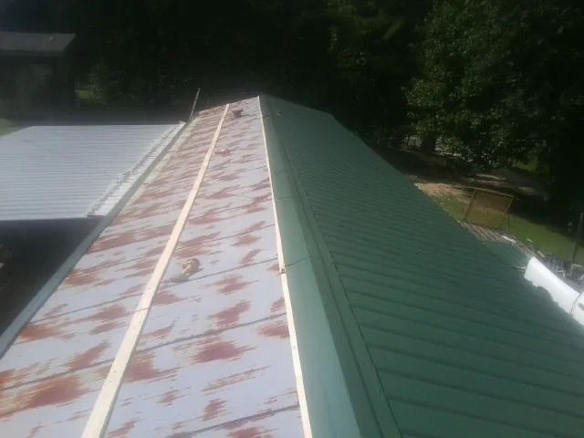 Old rusted panels beside newly installed green metal roofing — Wind Damage Roof Repair by Roofing Brothers in Anniston
