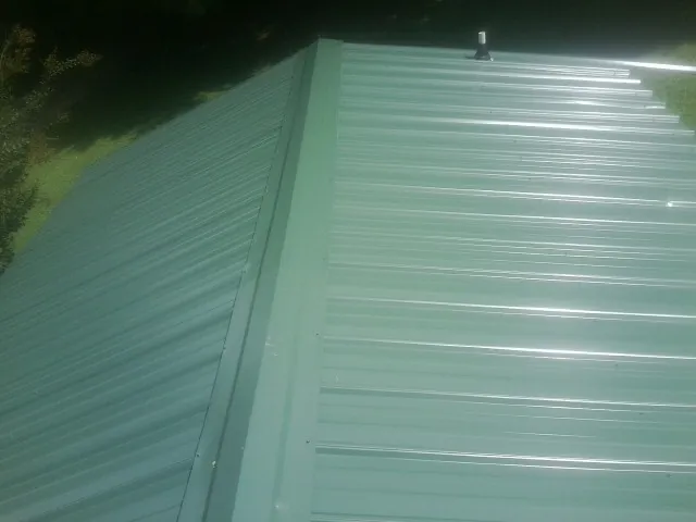 New green metal panels meeting at the ridge of a roof — Flat Roof Repair work by our crew in Anniston