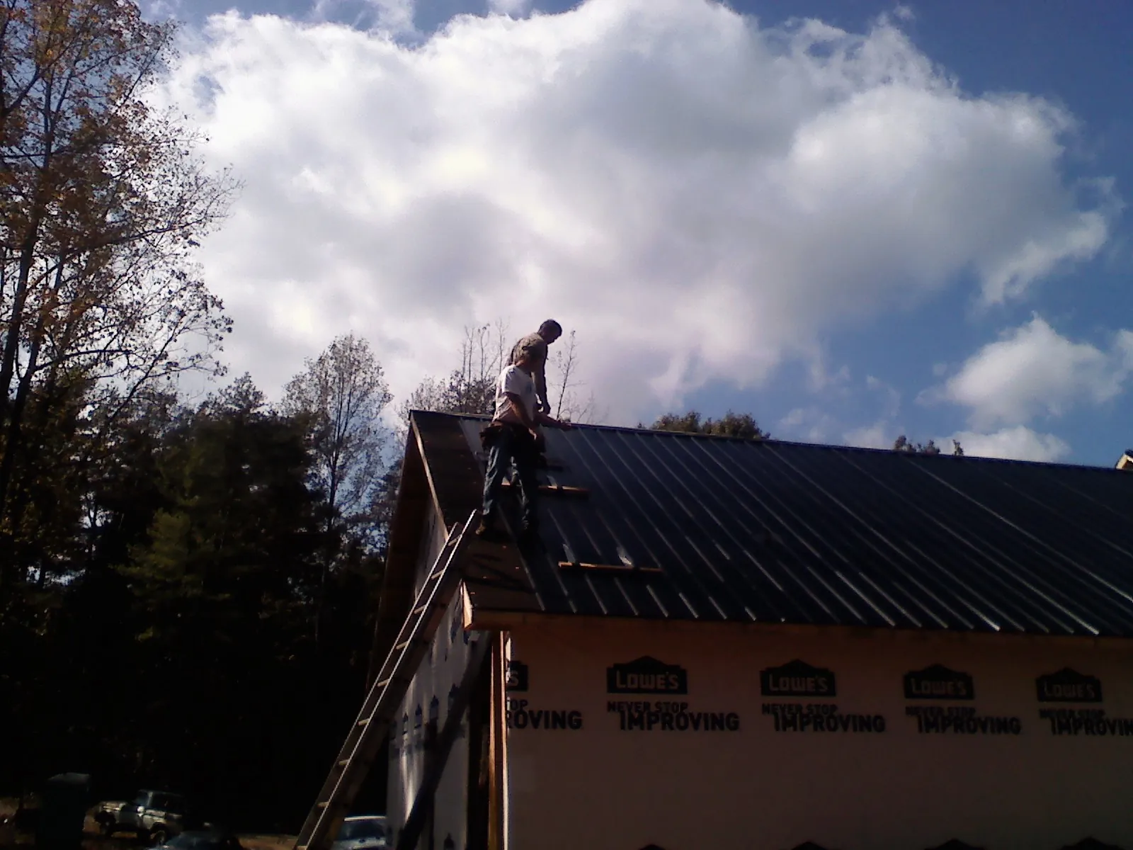 Roofer fastening dark metal panels high against a cloudy sky, from a Roof Inspection job in Anniston
