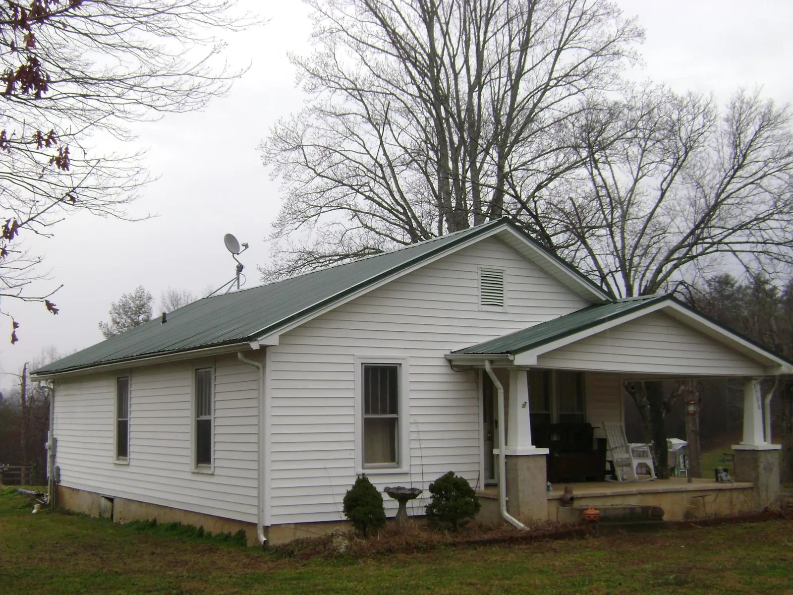Green metal roof on a white bungalow with a side porch in Anniston