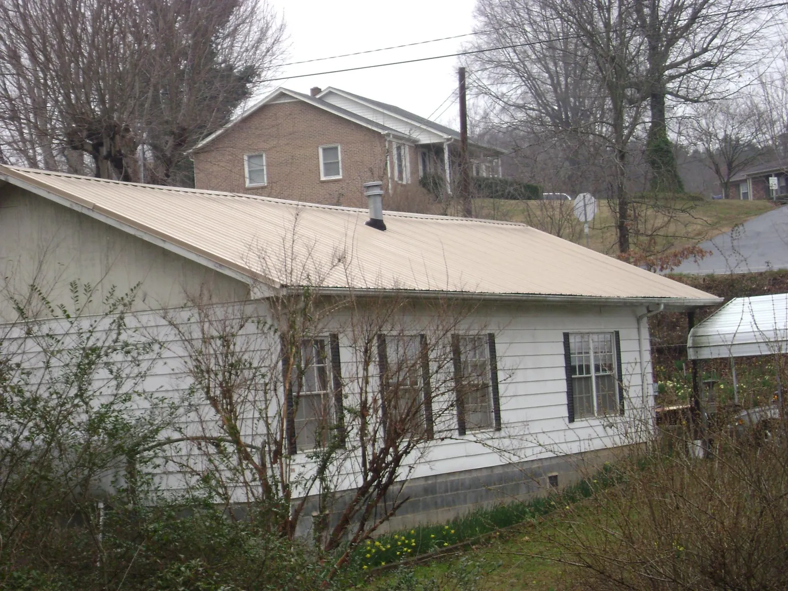 Tan metal roof on a white sided house set into a hillside — Commercial Roofing by Roofing Brothers in Anniston